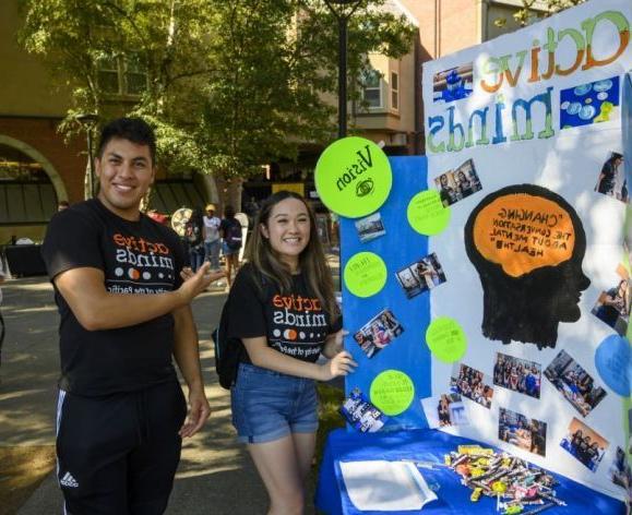 two students standing next to poster at club fair